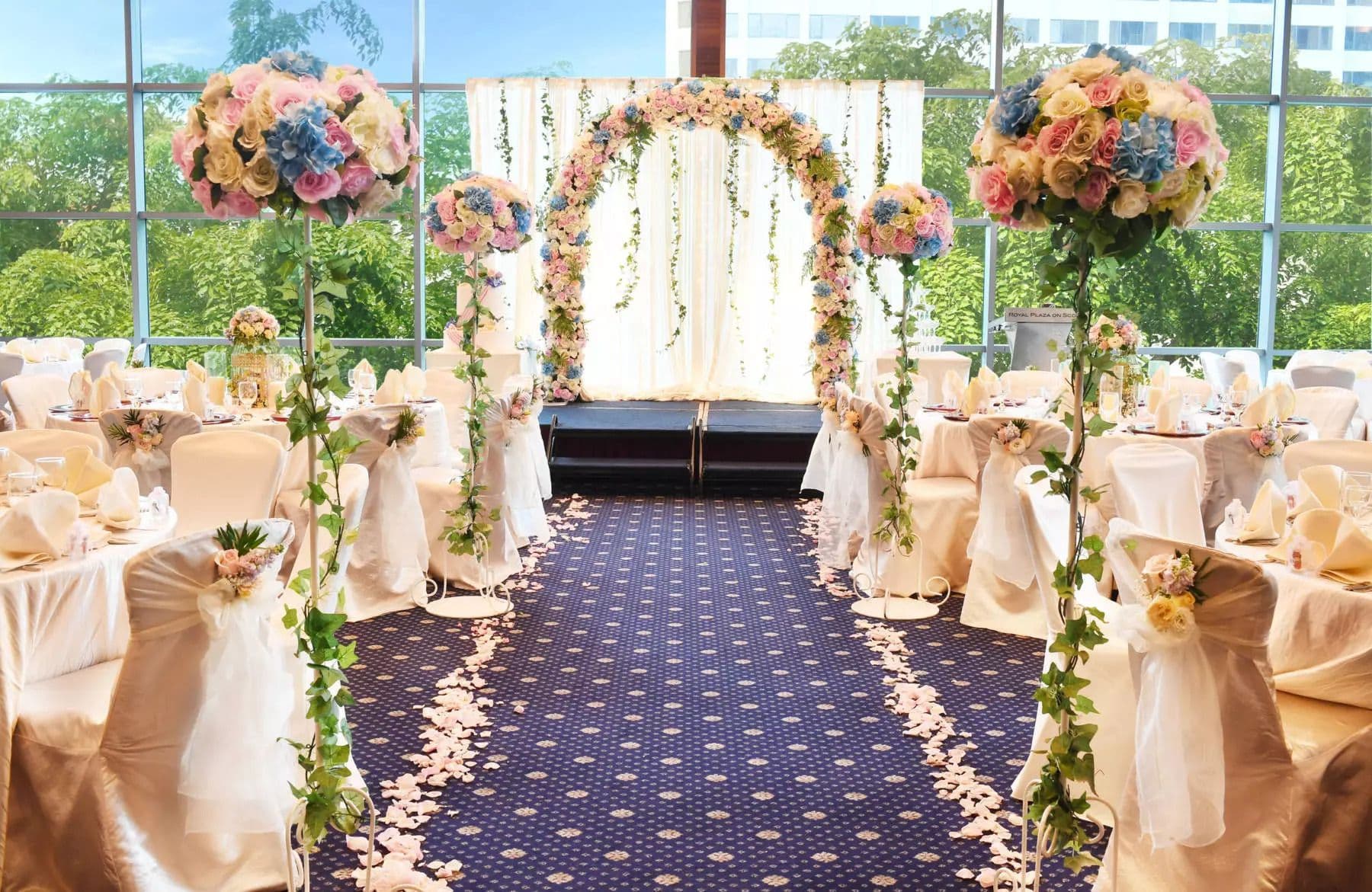 Elegant wedding reception hall featuring a floral arch, blue aisle, and white-draped tables.
