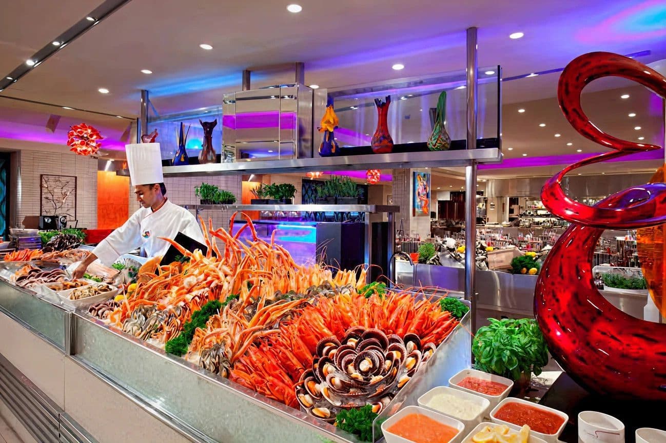 A chef serves fresh seafood at a luxurious buffet table with colorful ambient lighting.
