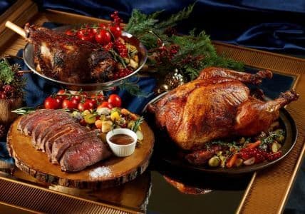A holiday feast features a roasted turkey, sliced prime rib, and a garnished leg of lamb.